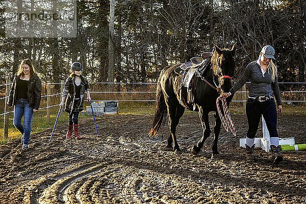 Ein junges Mädchen mit zerebraler Lähmung beendet ihre Hippotherapie-Sitzung mit ihrer Mutter und ihrem Trainer  der das Pferd führt; Westlock  Alberta  Kanada