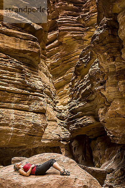 Ein Wanderer entspannt sich auf einem großen Felsen im Blacktail Canyon am Colorado River bei Meile 120 im Rahmen des Arizona Highways Photography Workshop; Grand Canyon National Park  Arizona  Vereinigte Staaten von Amerika