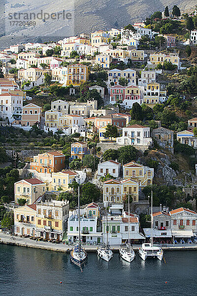 Überblick über pastellfarbene Gebäude und Segelboote  die entlang der Uferpromenade im Hafen von Gialos auf der Insel Symi (Simi) festgemacht sind; Dodekanes-Inselgruppe  Griechenland