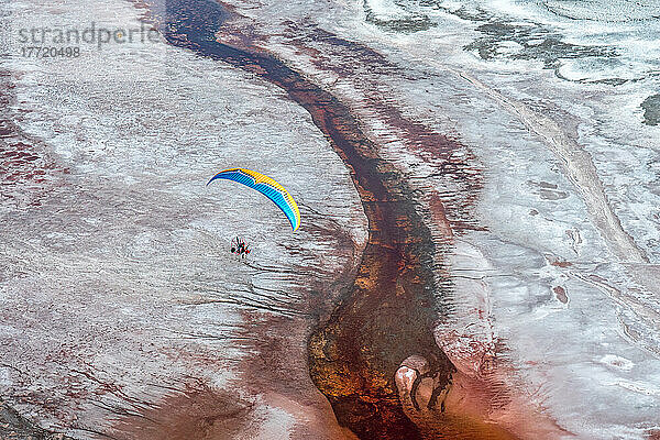 Ein Motorschirmpilot fliegt über den Owens Lake  einen größtenteils ausgetrockneten See in der Sierra Nevada in der Nähe von Lone Pine  wo salzliebende Halobakterien das seichte Wasser durch die salzigen Rückstände rot färben; Lone Pine  Inyo County  Kalifornien  Vereinigte Staaten von Amerika