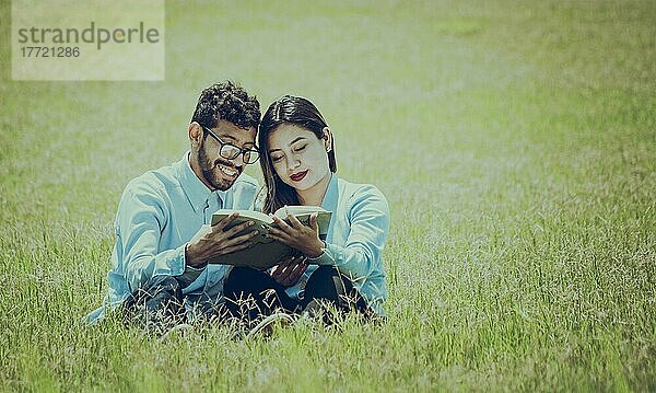 Zwei Menschen sitzen im Gras und lesen ein Buch  Konzept von Menschen  die draußen lesen  Ein Paar sitzt im Gras und liest ein Buch
