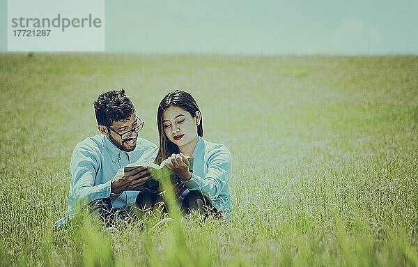 Ein Paar  das im Gras sitzt und ein Buch liest  Zwei Menschen  die im Gras sitzen und ein Buch lesen  Konzept von Menschen  die draußen lesen