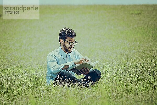 Junger Mann im Gras  der ein Buch liest  Eine Person  die im Gras sitzt und ein Buch liest  Konzept von Menschen  die draußen lesen