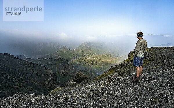 Wanderer blickt in die Ferne  Ausblick auf zerklüftete Berge und Täler  Tal mit Fluss Hrauná  vulkanische Landschaft am Wanderweg Fimmvörðuháls  Þórsmörk Nature Reserve  Suðurland  Island  Europa