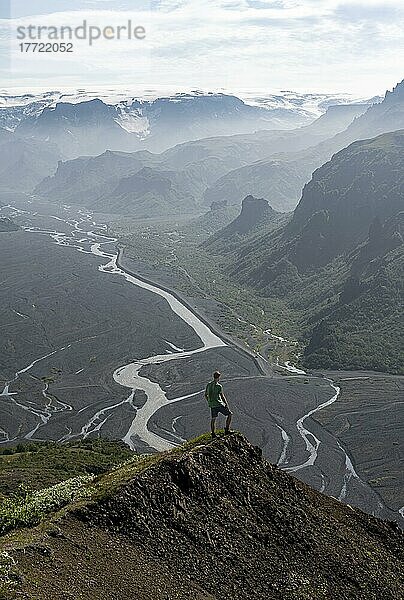 Wanderer am Gipfel des Valhanúkur  Blick auf Bergtal mit mäanderndem Fluss Krossá  zerklüftete Berglandschaft  hinten Gletscher Myrdalsjökull  Þórsmörk Nature Reserve  Suðurland  Island  Europa