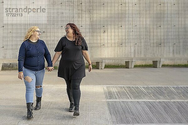 Latin lesbischen Paar Blick auf einander mit Zuneigung zu Fuß Hand in Hand auf der Straße