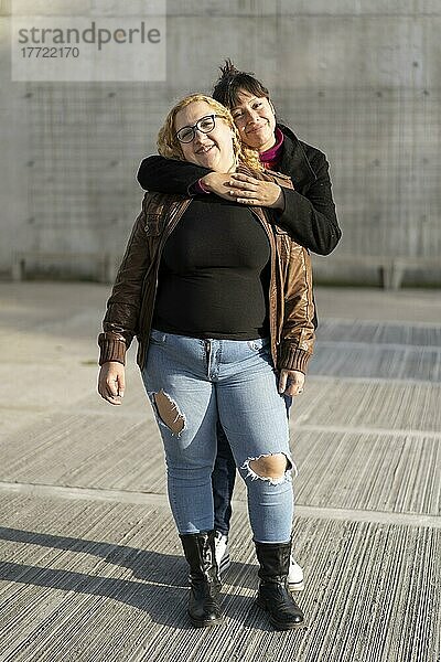 Ein Paar lesbischer Fraün umarmt sich in einem Park und schaut lächelnd in die Kamera. Raum kopieren