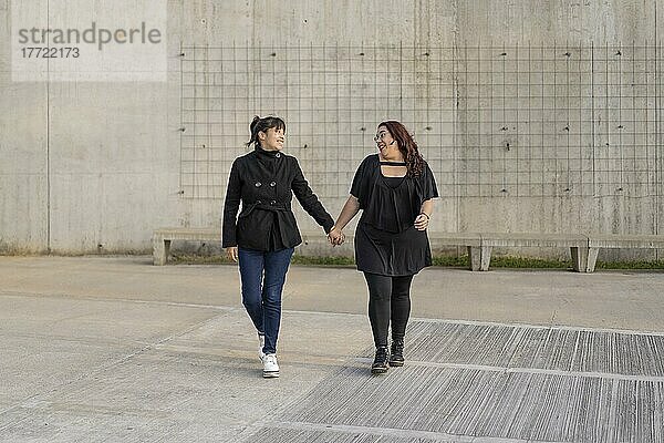 Lateinisches lesbisches Paar  das sich liebevoll anschaut und Hand in Hand auf der Straße geht. Raum kopieren
