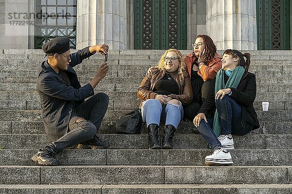 Eine multiethnische Gruppe von Freunden sitzt auf einer Treppe und unterhält sich  lacht und macht Fotos