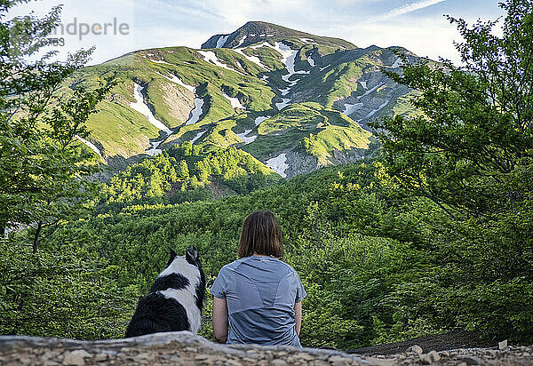 A girl sitting beside her border collie dog staring at a mountain landscape of Cusna Mountain  Emilia Romagna  Italy  Europe