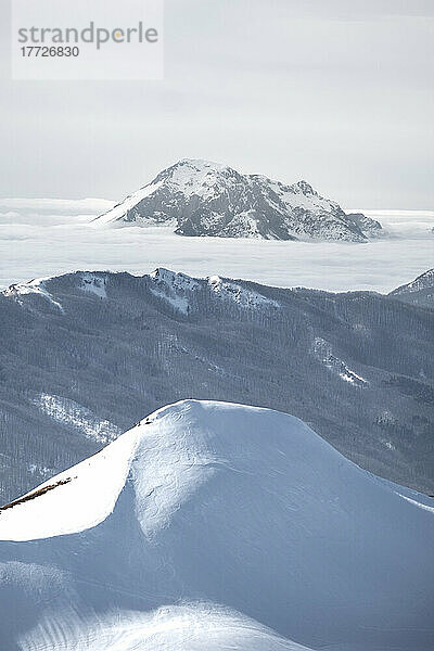 Schneebedeckter Berg  der aus Nebel im Hintergrund und schneebedecktem Hügel im Vordergrund auftaucht  Emilia Romagna  Italien  Europa