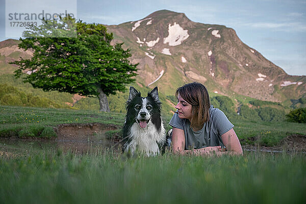 A girl and her border collie dog lying in the grass with a tree and mountain in the background  Emilia Romagna  Italy  Europe