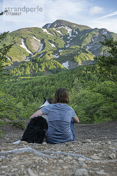 A girl sitting beside and hugging her border collie dog staring at a mountain landscape of Cusna Mountain  Emilia Romagna  Italy  Europe