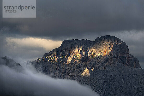 Sunset on Croda Rossa d'Ampezzo mountains surrounded by the fog and darkness with only a few spots of sun light  Dolomites  Veneto  Italy  Europe