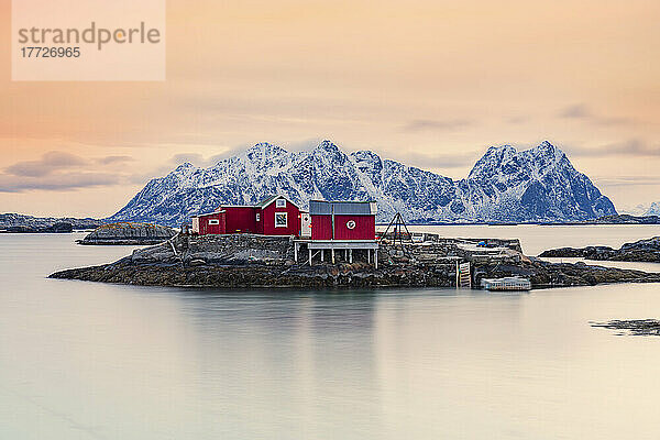 Isolierte rote Fischerhütten auf Felsen im kalten Meer bei Sonnenuntergang  Svolvaer  Kreis Nordland  Lofoten  Norwegen  Skandinavien  Europa