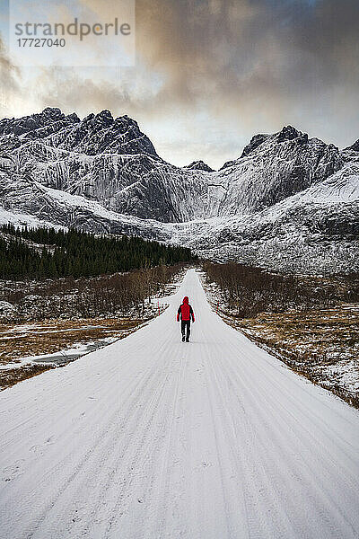 Mann läuft im Winter auf einer leeren  schneebedeckten Bergstraße  Nusfjord  Kreis Nordland  Lofoten  Norwegen  Skandinavien  Europa