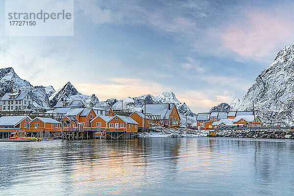 Mit Schnee bedeckte Fischerhütten aus Holz bei Sonnenuntergang im winzigen Dorf Sakrisoy  Reine  Nordland  Lofoten  Norwegen  Skandinavien  Europa