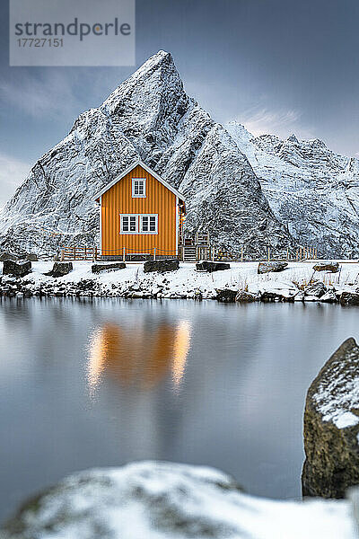 Rorbu im Schnee am Fuße des Olstind-Berges mit Blick auf das Arktische Meer  Sakrisoy  Reine  Nordland  Lofoten-Inseln  Norwegen  Skandinavien  Europa