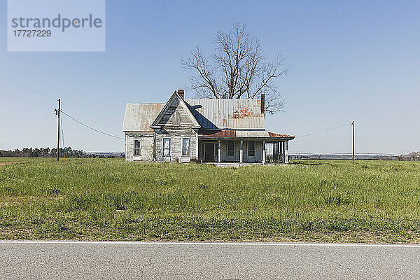 Verlassenes Haus mit rostigem Blechdach in einem Ackerland an einer Straße.