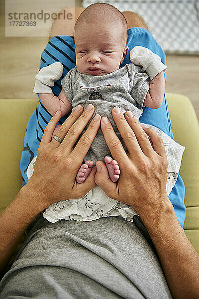 Draufsicht auf die Hände des Vaters  die auf dem schlafenden drei Monate alten Jungen mit Handschuhen ruhen