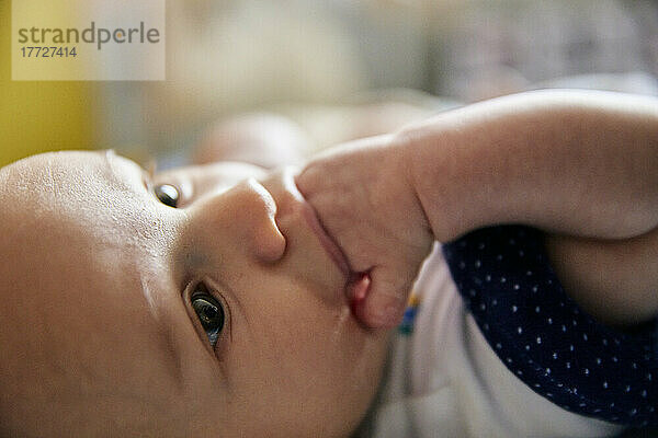Nahaufnahme eines drei Monate alten Babyjungen  der sich hinlegt und an seinen Fingern saugt