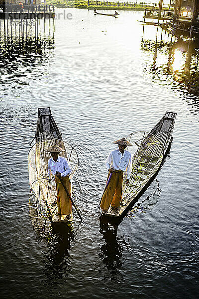 Zwei Fischer auf traditionellen Booten auf dem See mit Fischernetzen.