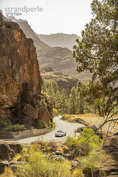 Blick auf ein Auto  das durch eine bergige Landschaft in der Nähe von Barranco de Mogan fährt  in der Nähe des Dorfes Mogan  Gran Canaria  Kanarische Inseln  Spanien  Atlantik  Europa