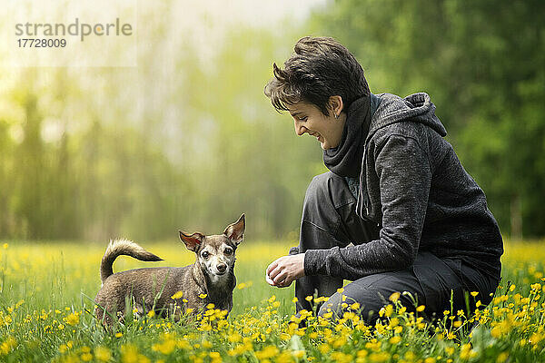 Kleiner Hund und sein Besitzer hockten auf einem Feld voller gelber Blumen  Italien  Europa
