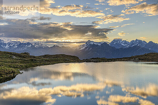 Die Sonne und die Wolken spiegeln sich bei Sonnenaufgang im Arcoglio-See  Valmalenco  Valtellina  Lombardei  Italien  Europa