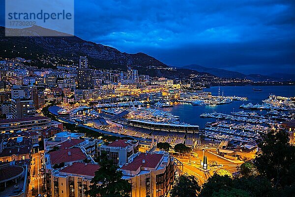 Luftaufnahme des Hafens von Monaco Monte Carlo und der beleuchteten Skyline der Stadt in der abendlichen blauen Dämmerung. Monaco Hafen Nachtansicht mit luxuriösen Yachten