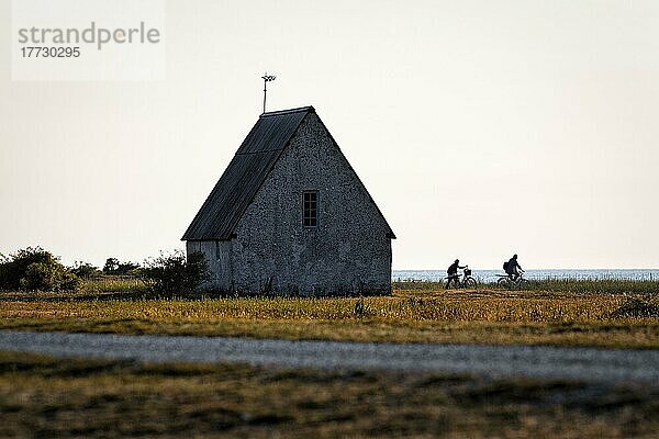 Kleine Fischerkapelle auf einer Wiese  Gegenlicht  Silhouetten von zwei Radfahrern  Kovik Fischereimuseum  Westküste der Insel Gotland  Ostsee  Schweden  Europa