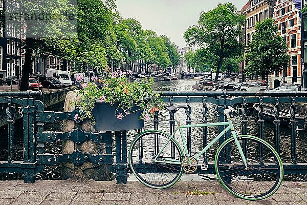 Typische Amsterdamer Ansicht  Amsterdamer Gracht mit Booten und geparkten Fahrrädern auf einer Brücke mit Blumen. Amsterdam  Niederlande  Europa