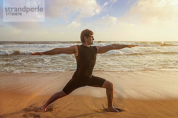 Mann macht Hatha Yoga Asana Virabhadrasana 1 Warrior Pose im Freien am Strand bei Sonnenuntergang. Kerala  Indien  Asien