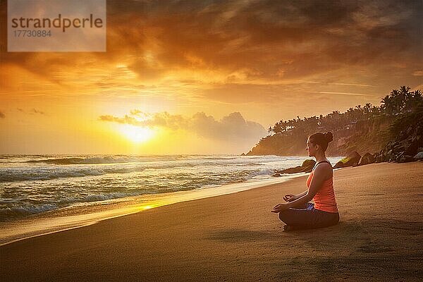 Junge sportliche  fitte Frau macht Yoga  meditiert und entspannt sich in Padmasana Lotus Pose) mit Kinn Mudra im Freien am tropischen Strand bei Sonnenuntergang