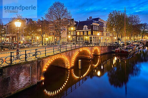 Nachtansicht der Stadt Amsterdam mit Gracht  Brücke und mittelalterlichen Häusern in der Abenddämmerung beleuchtet. Amsterdam  Niederlande  Europa