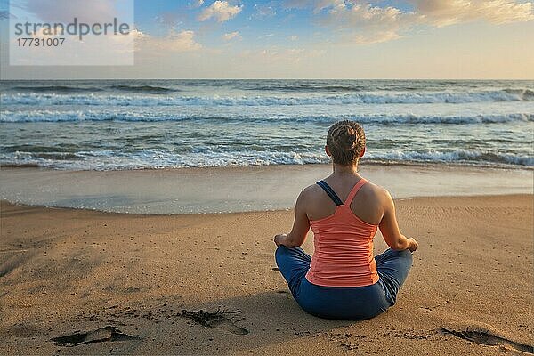 Frau macht Yoga  meditiert und entspannt in Padmasana Lotus Asana Pose mit Kinn Mudra im Freien am tropischen Strand bei Sonnenuntergang