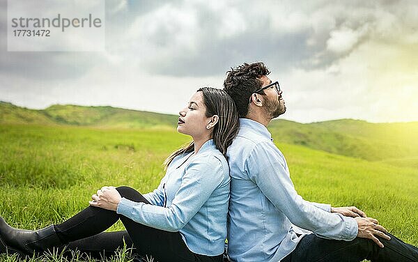 Ein Paar sitzt mit dem Rücken zueinander im Gras  ein Hochzeitspaar auf dem Feld sitzt mit dem Rücken zueinander und schaut in die Kamera
