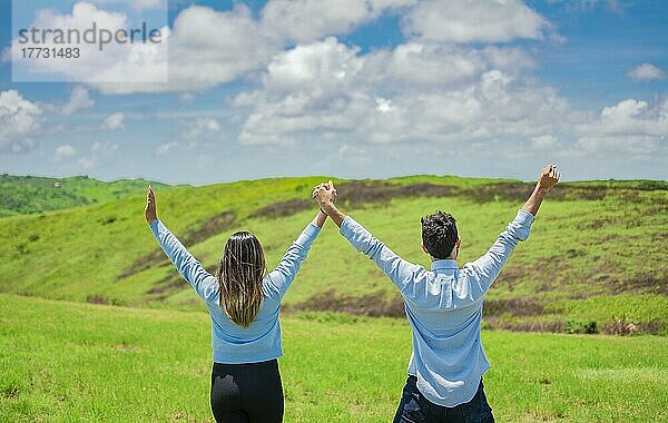 Rückenansicht eines glücklichen Paares auf dem Feld  das die Hände zum Himmel hebt  Konzept eines glücklichen und freien Paares auf dem Feld  Rückenansicht eines Paares auf dem Hügel mit zum Himmel erhobenen Händen
