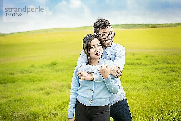 Porträt eines glücklichen Paares  das sich auf dem Feld umarmt  Porträt eines jungen verliebten Paares auf der grünen Wiese  das in die Kamera schaut  Porträt eines niedlichen Paares auf dem Feld