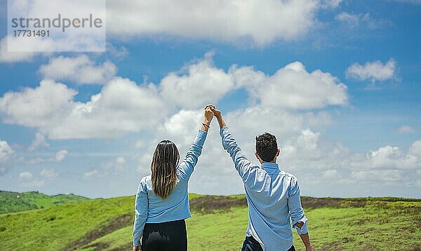 Rückenansicht eines Paares auf dem Hügel mit zum Himmel erhobenen Händen  Glückliches Paar auf dem Feld  das die Hände in den Himmel streckt  Konzept eines glücklichen und freien Paares auf dem Feld