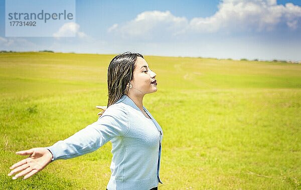 Glückliche Frau atmet frische Luft auf dem Feld und breitet die Arme aus  junge Frau lächelt und breitet ihre Hände auf der grünen Wiese aus  Konzept der Frau atmet frische Luft auf dem Feld