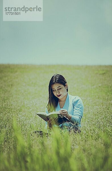 Eine Person sitzt im Gras und liest ein Buch  Attraktive Menschen sitzen im Gras und lesen ein Buch  Ein Mädchen liest ein Buch im Feld