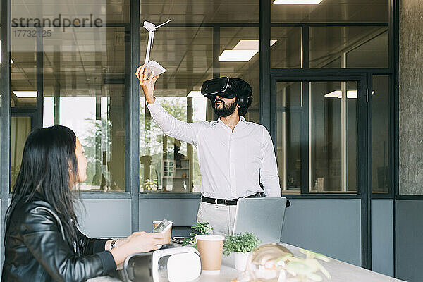 Geschäftsmann mit VR-Brille hält Windturbinenmodell von Kollege am Arbeitsplatz