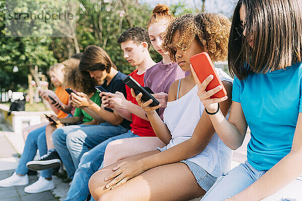 Gemischtrassige Freunde nutzen an sonnigen Tagen Mobiltelefone