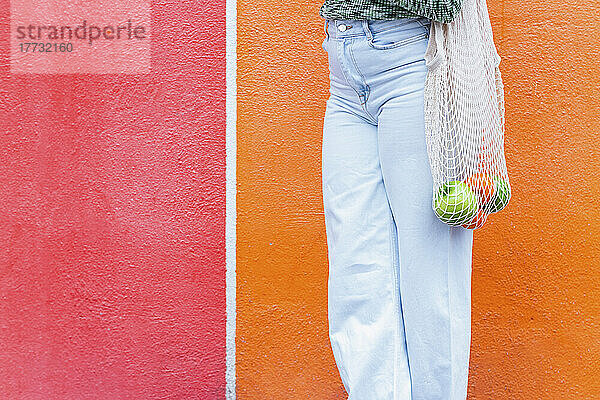 Frau mit einer Tüte Obst steht vor einer roten und orangefarbenen Wand