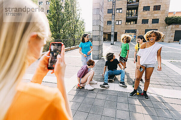 Girl with smart phone photographing friends having fun at parking lot