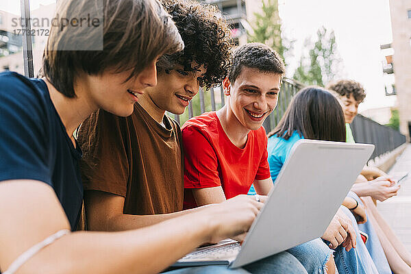 Fröhliche Jungs  die sich gemeinsam mit Freunden einen Laptop teilen