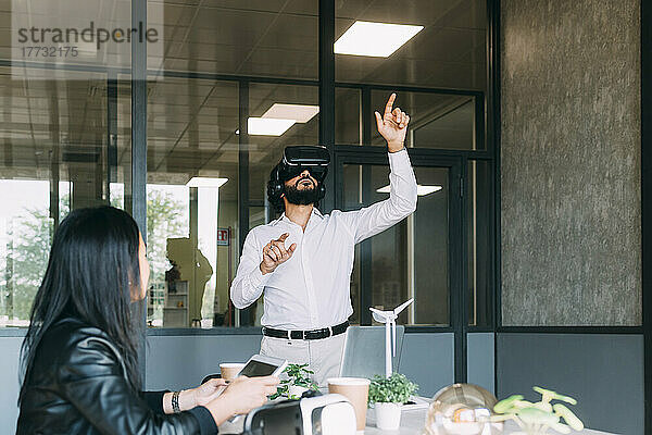 Geschäftsmann gestikuliert mit VR-Brille von einem Kollegen im Büro