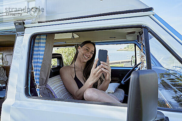 Glückliche Frau bei Videoanruf über Smartphone im Wohnmobil