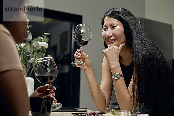 Glückliche Frau hält Weinglas und spricht zu Hause mit ihrer Freundin